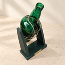 Angled view of the green glass bottle in its dark-green stand and curved metal cradle.