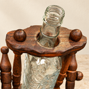 Close-up of the nautical bottle holder's scalloped upper frame, wooden finials and clear bottle neck.